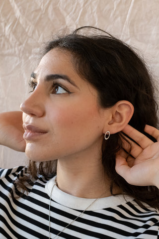 Woman wearing a black and white striped shirt, adjusting the Aurelia nile and nova earring against a beige wall.