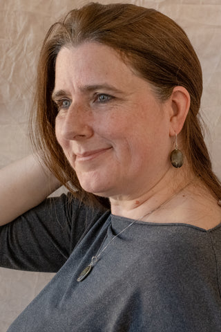 Woman wearing Noira sterling silver stone drop earrings and matching pendant necklace, smiling in side profile with hand in hair against a neutral backdrop.