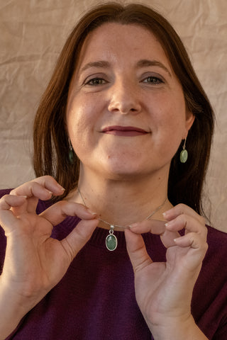 Sterling silver Selva necklace with green oval pendant held by model wearing burgundy top by Nile & Nova