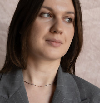 Woman wearing a gray suit with a neutral background. Silver thin chain on her neck.