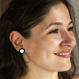 Side profile of a smiling woman wearing round black and silver stud earrings with a polished finish.