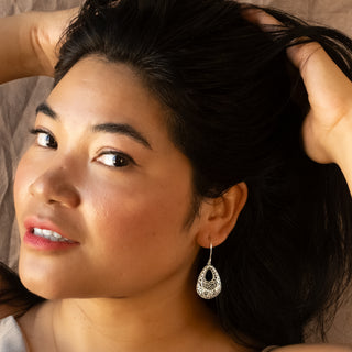 Model reclining gracefully, wearing the Lace Drop earrings by Nile & Nova — elegant silver filigree drops with soft shine.